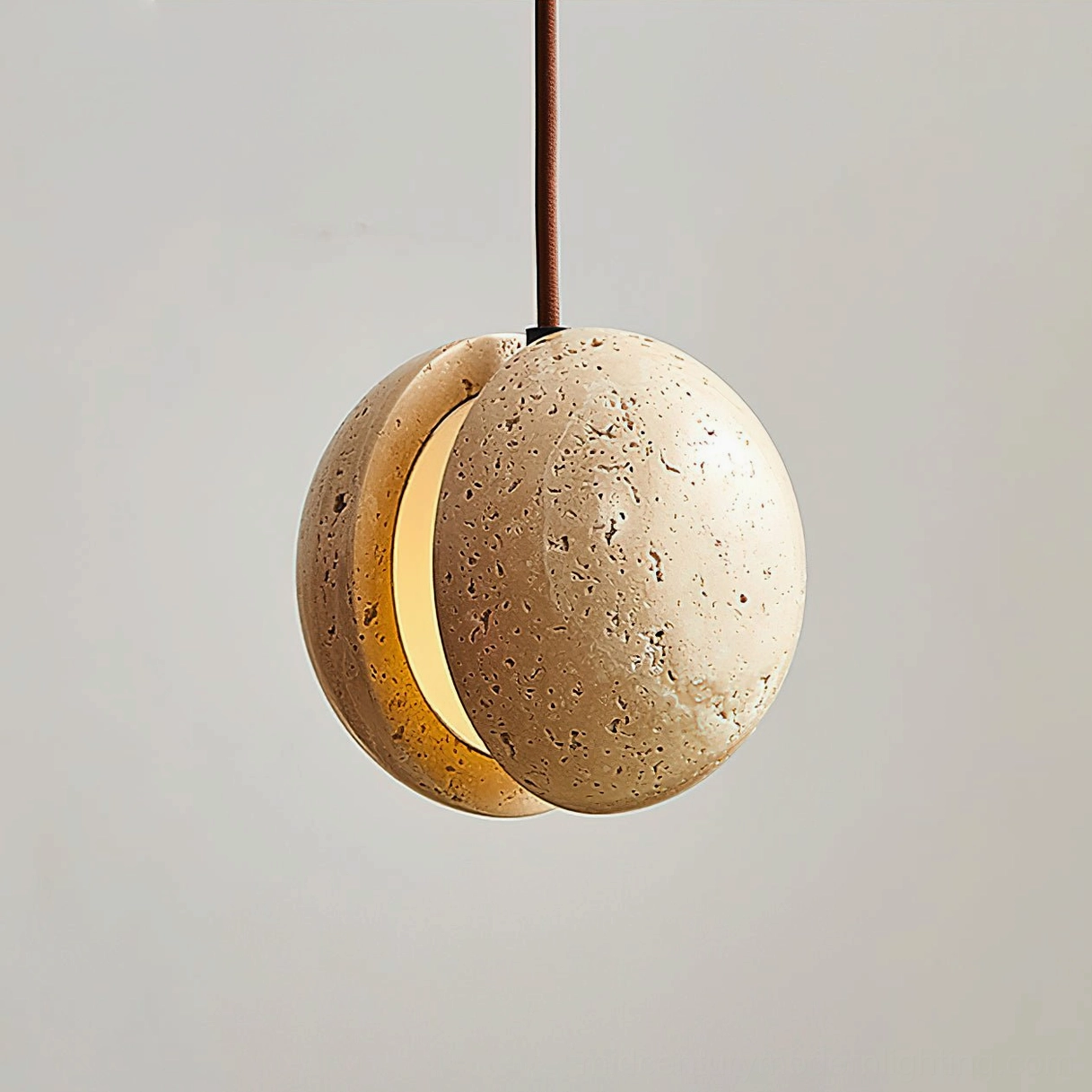 Wisteria travertine split-sphere pendant lamp close-up detail showing porous stone surface and crescent light aperture, studio shot