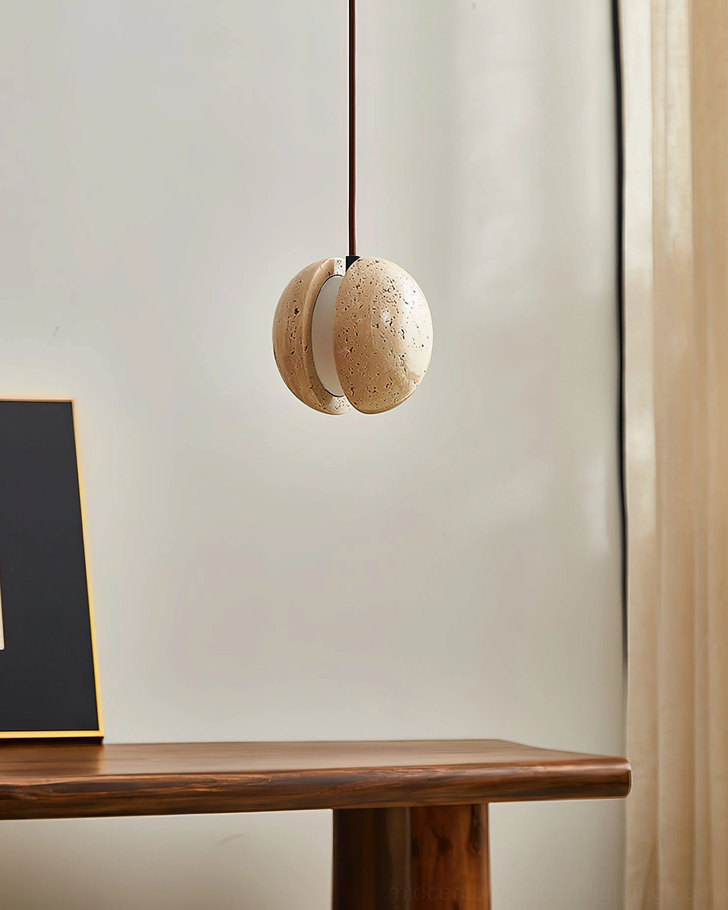 Wisteria travertine pendant lamp unlit side view, compact spherical form, console table with framed art decor
