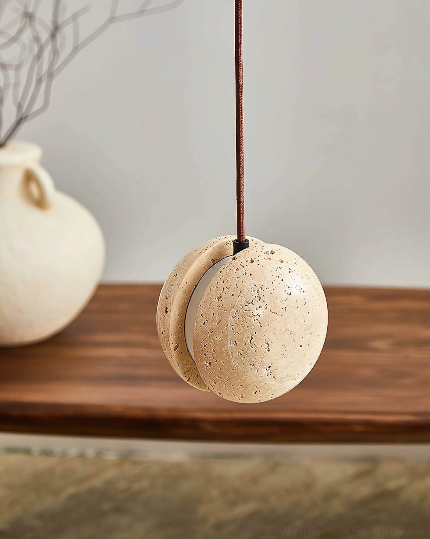 Wisteria travertine pendant lamp lit close-up showing split-sphere design and crescent light gap, dining area setting