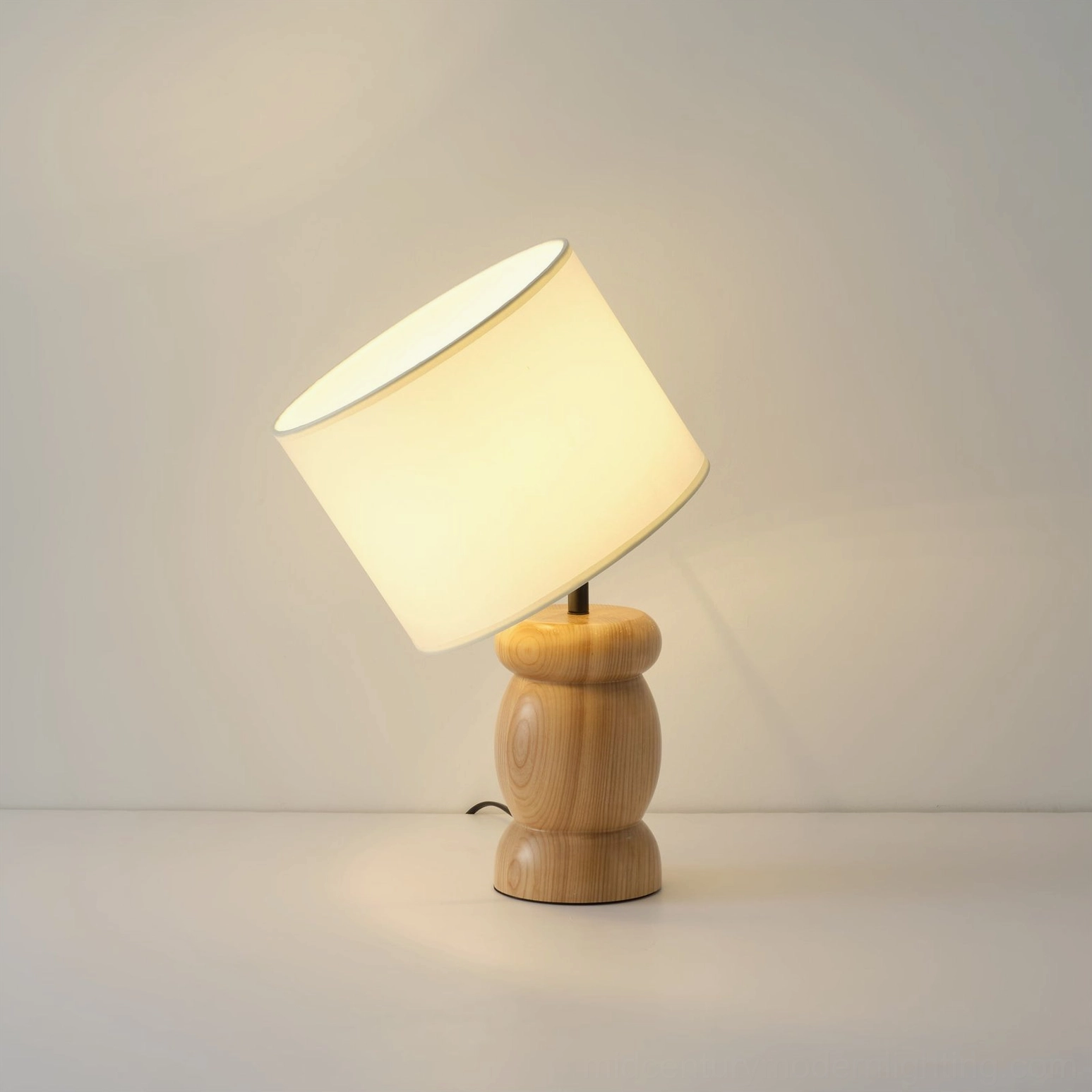 Wooden desk lamp with tilted off-white fabric shade, low side angle view showing sculptural wood base, soft warm glow