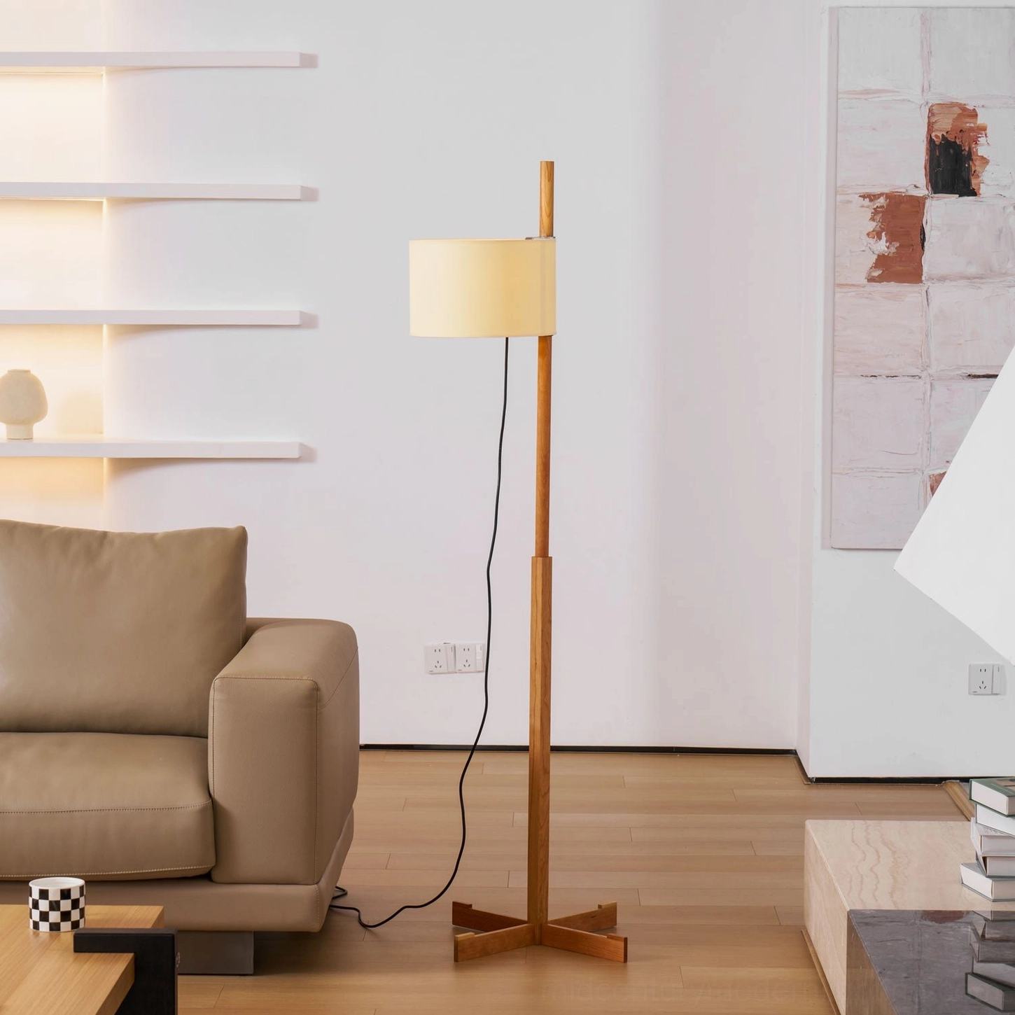 Wooden floor lamp illuminated beside table with stacked books in minimalist interior