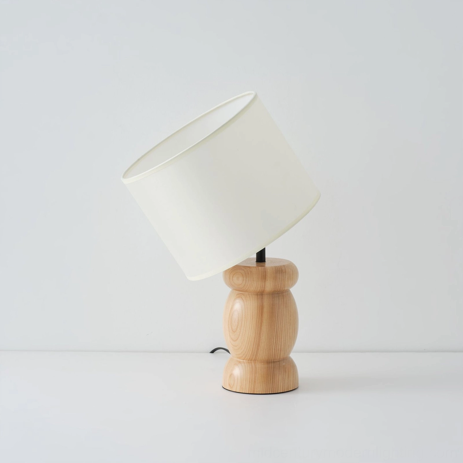 Wooden table lamp with tilted shade from low side perspective, soft illumination, sculptural wood base, studio setting