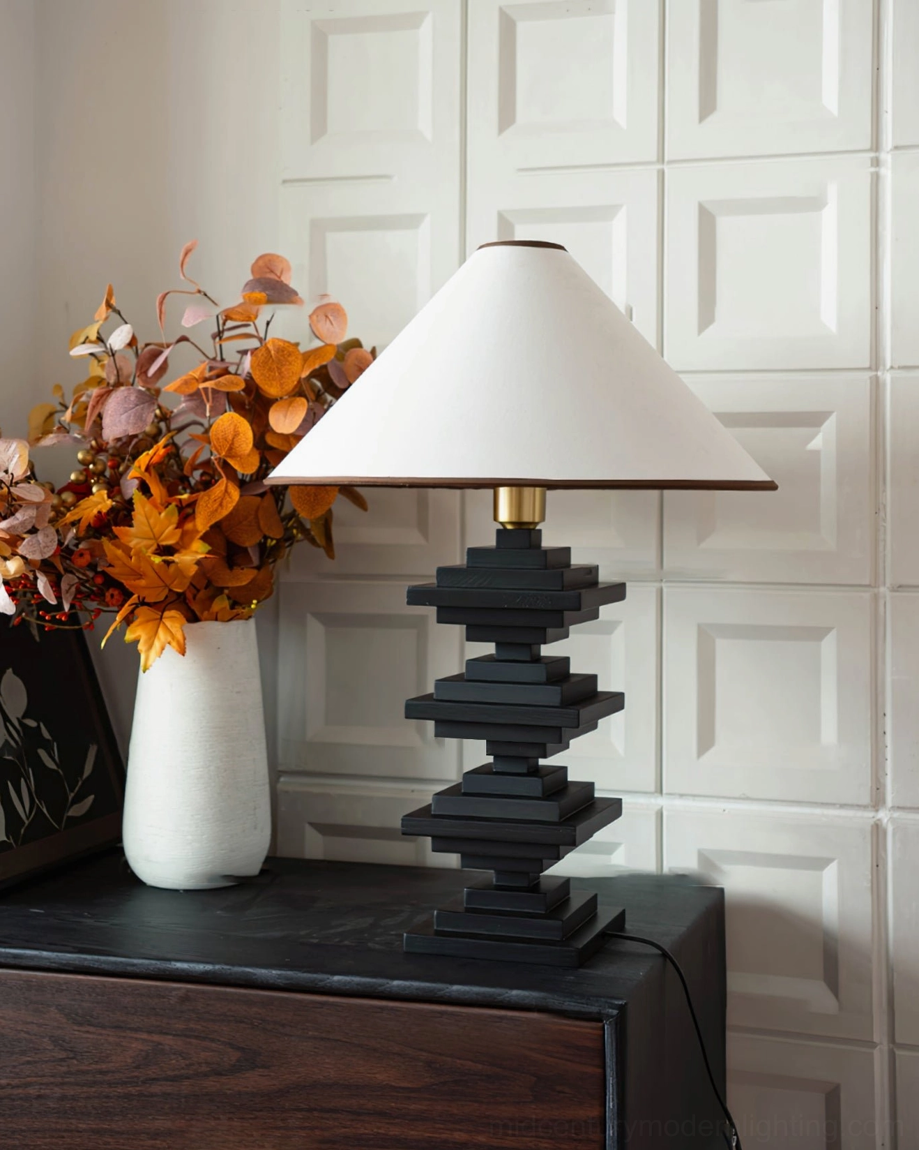 Wooden stacked tower lamp side three-quarter angle on dark dresser with autumn floral styling