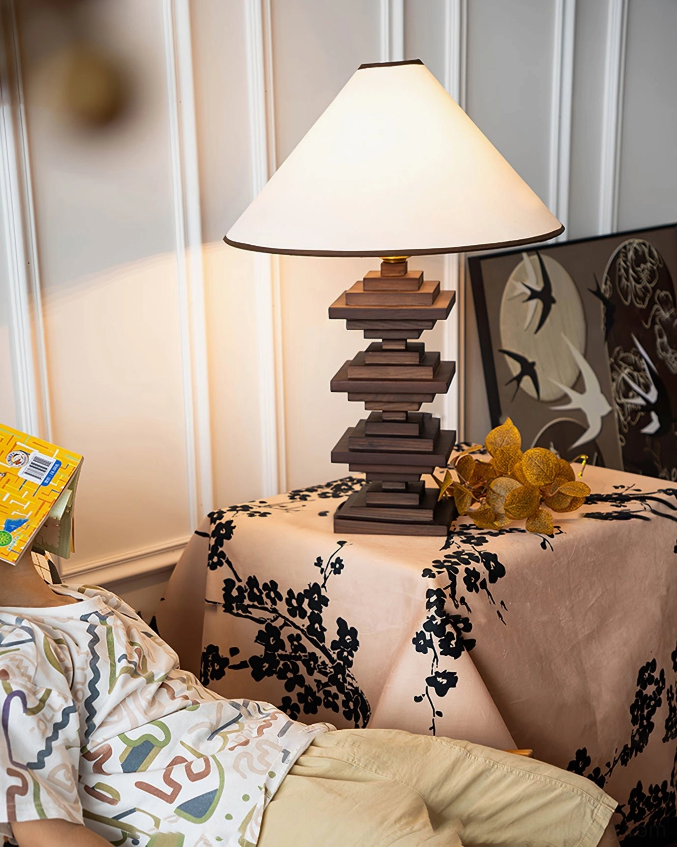 Stacked wood tower table lamp in cozy bedroom setting with dried flower decor and textile elements