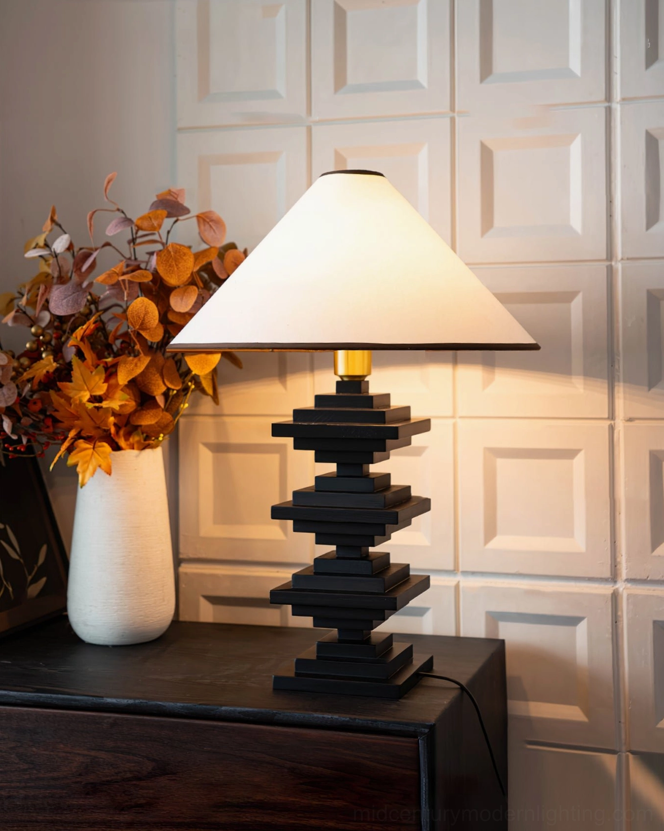 Dark wood tower lamp with autumn dried floral arrangement on dresser with grid wall panels