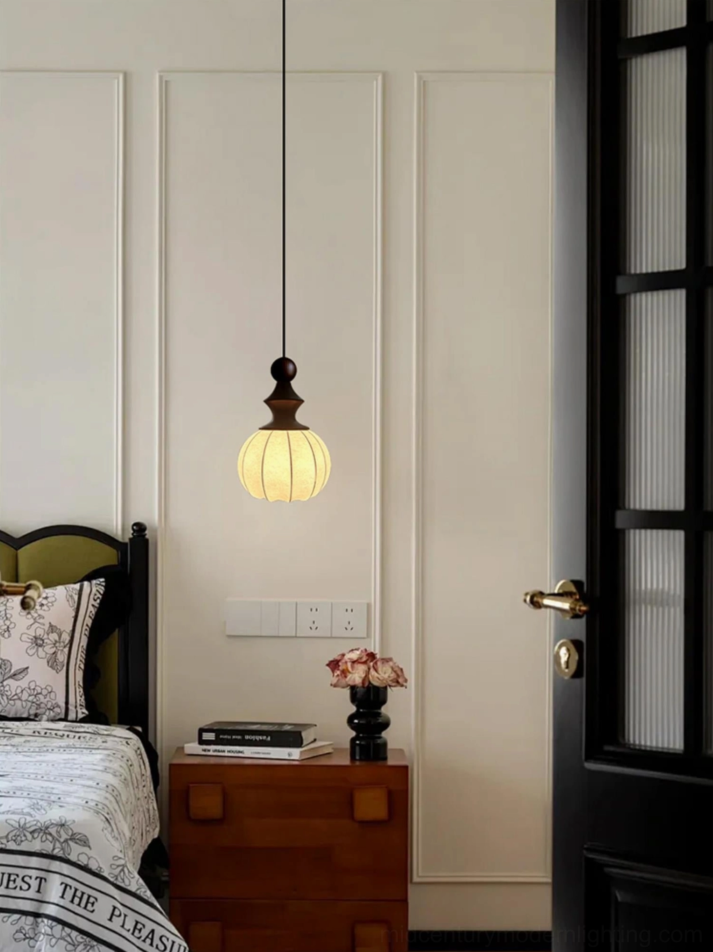 Wooden fabric pendant light mounted in mid-century modern bedroom next to dark wood nightstand and black door frame