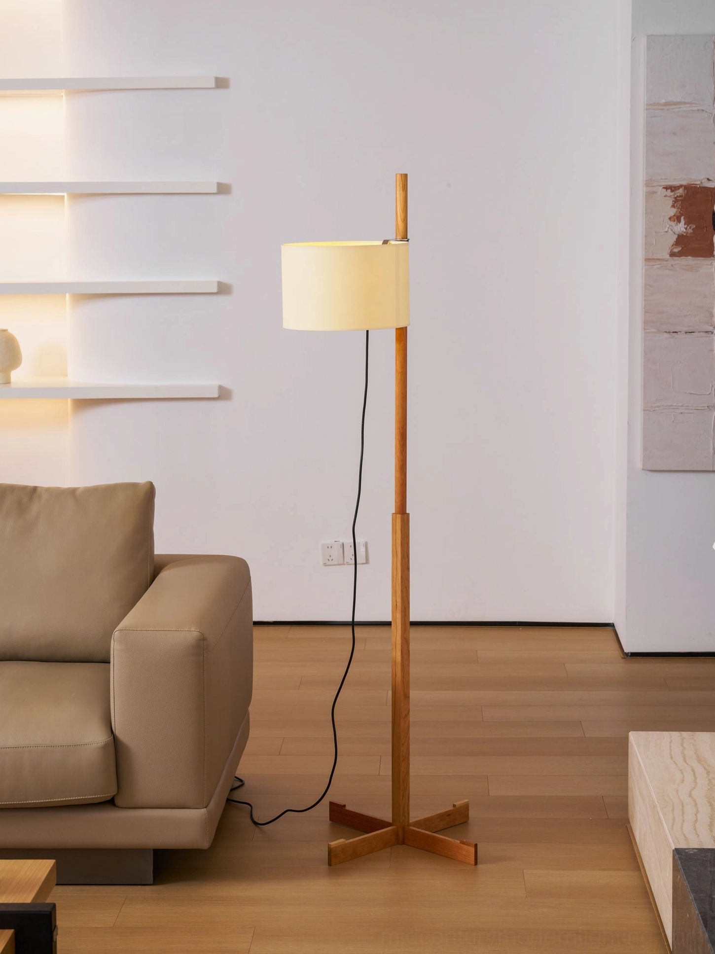 Illuminated wooden floor lamp beside leather sofa in contemporary living room with wall shelves