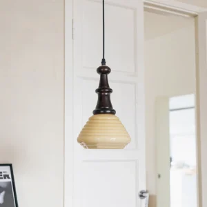 Wooden pendant light installed in modern home entryway with warm yellow illumination and black hanging cord, side angle view