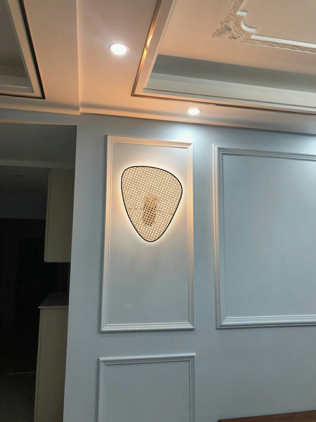Single woven rattan wall lamp in modern hallway with paneled walls and recessed ceiling lights contemporary installation
