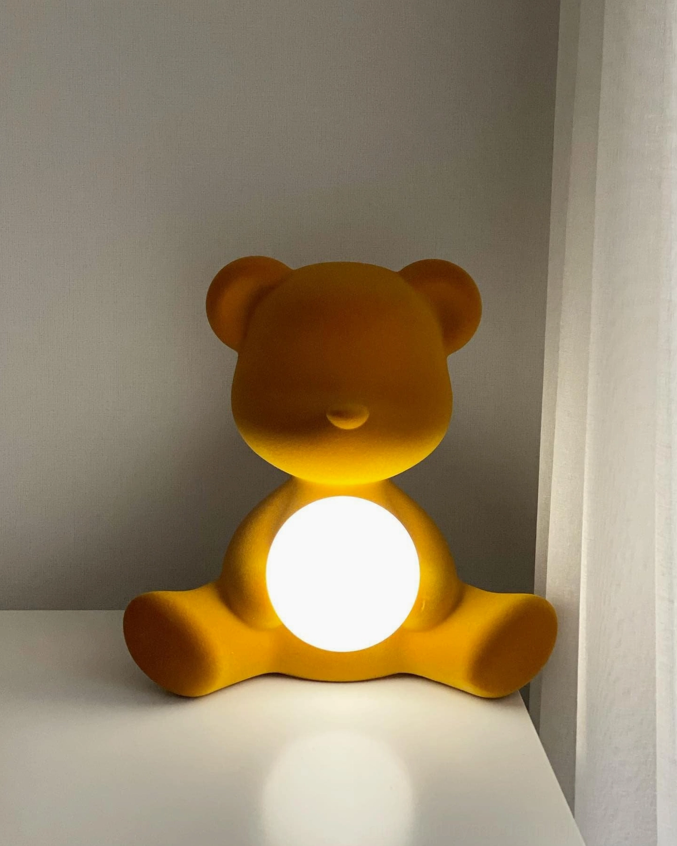 Yellow teddy bear table lamp with warm glowing light on minimalist bedroom desk