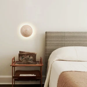 Travertine wall sconce mounted in modern bedroom with upholstered headboard creating warm ambient glow