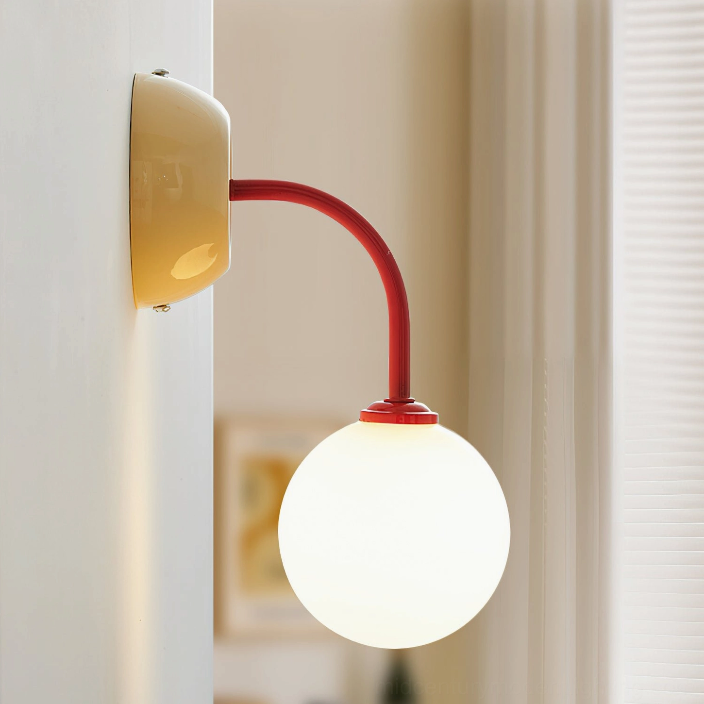 Zesta modern wall lamp side profile view, cream yellow metal base with frosted glass globe, mounted on bedroom wall with sheer curtain backdrop