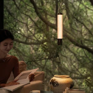 Zigrina pendant light illuminating outdoor lounge area with woman reading under tree canopy warm ambient glow