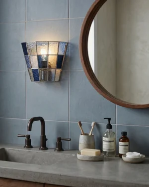 Navy blue stained glass wall sconce installed in modern grey tile bathroom as vanity lighting