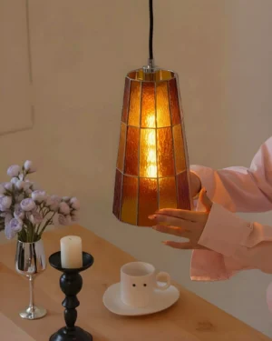 Zola stained glass pendant lamp illuminated above dining table with warm amber glow, mid-century modern interior setting